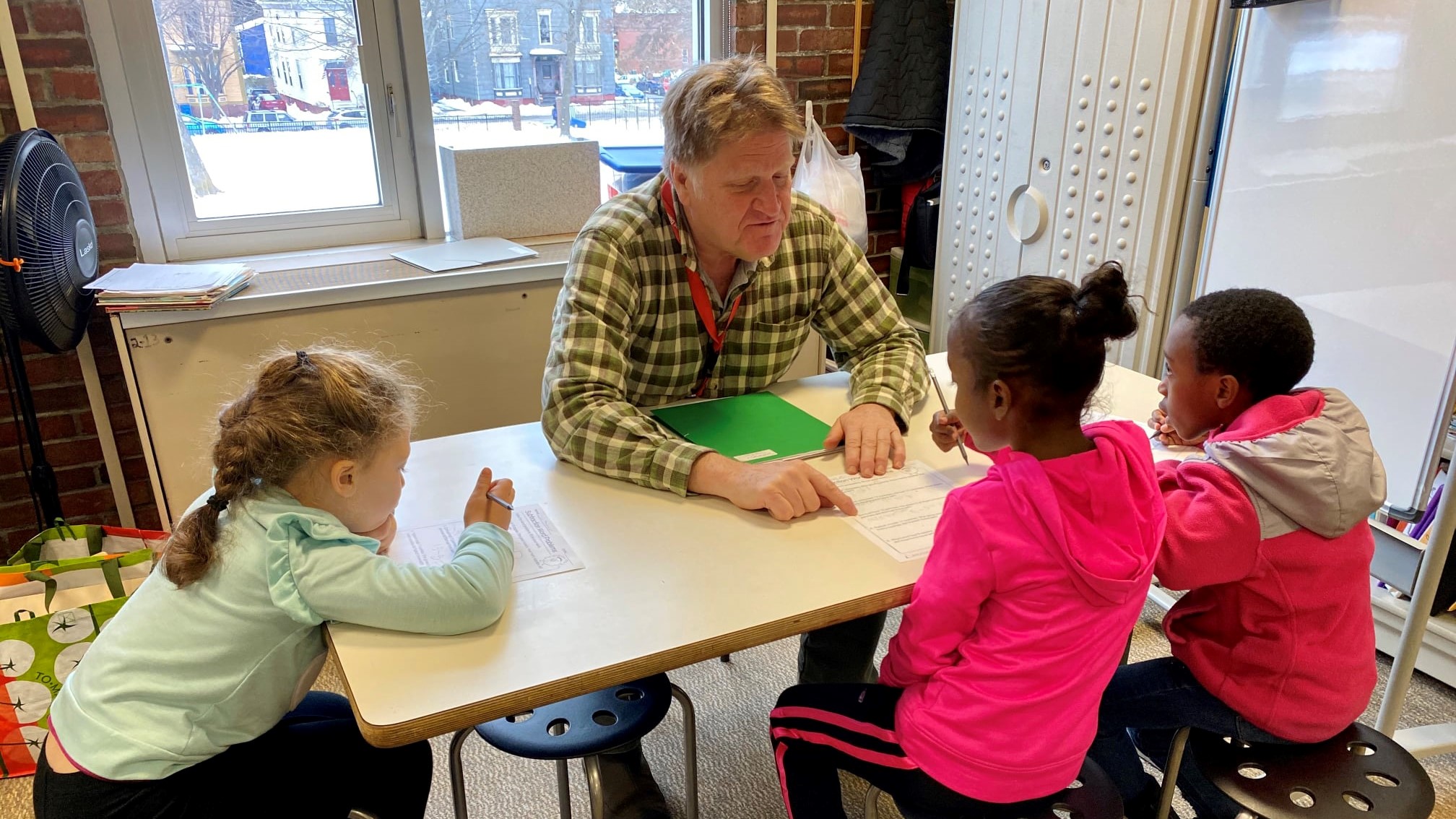 A teacher reads to three children at a table inside a classroom
