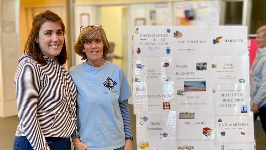 Left to right: Heather and Kris Galasyn pose for a photo inside the First Parish Church in Saco next to an information board that includes details on services available during the MLK Day of Service activity.
