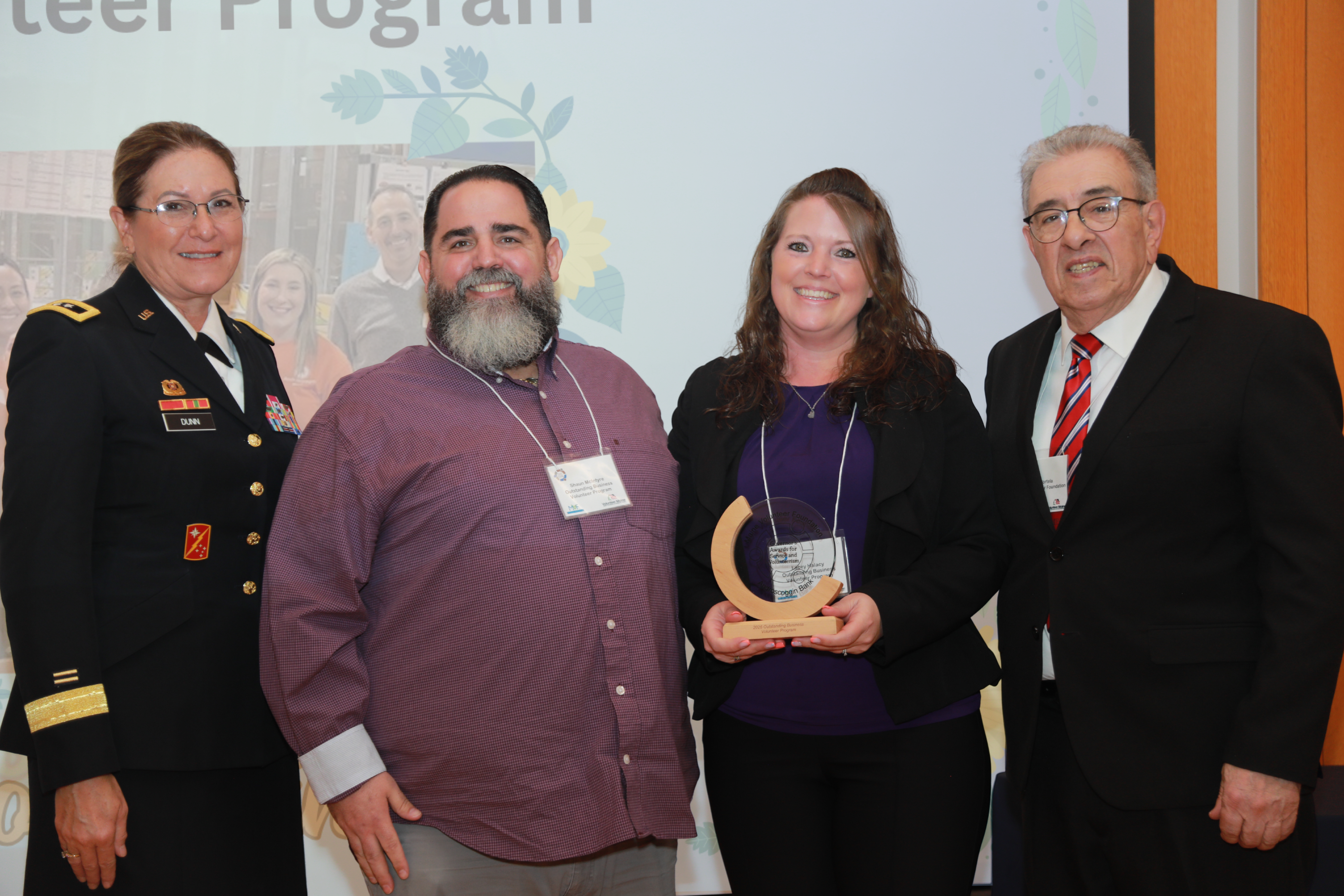 Representatives from Androscoggin Bank hold a crescent wood and glass award and stand between Major General Diane Dunn and Maine Volunteer Foundation President John Portela