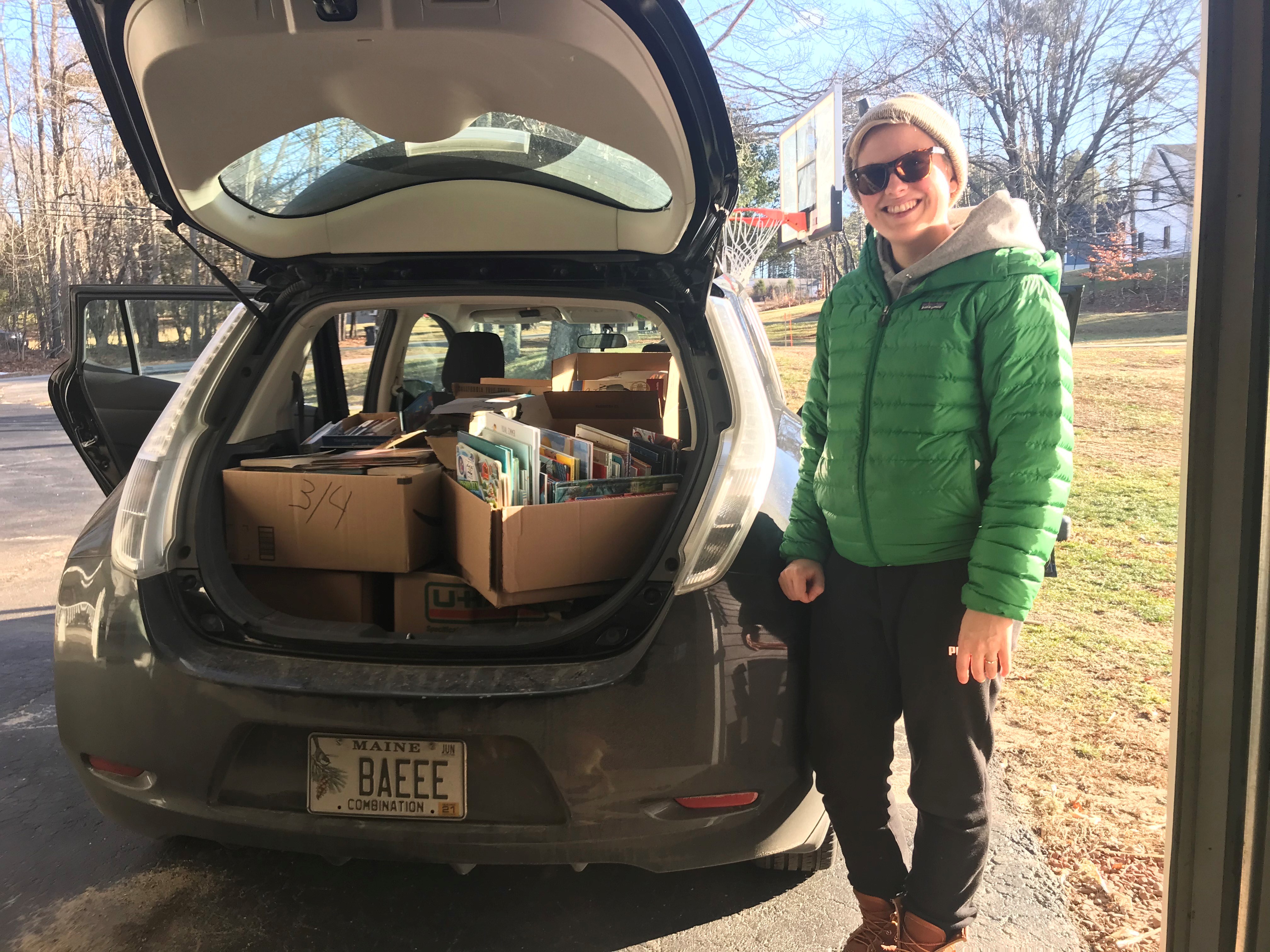 Person standing by a car with an open trunk full of books