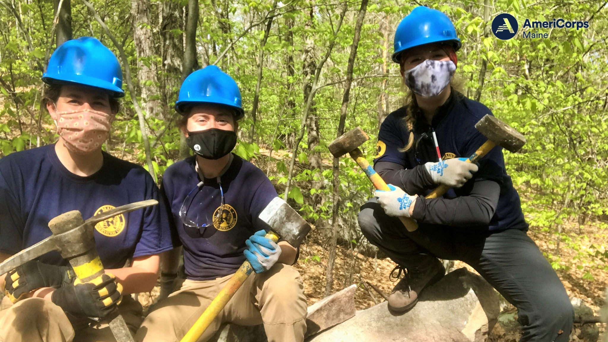 Three individuals pose in the woods with trail maintenance gear and equipment