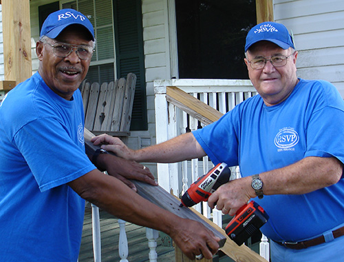 two adult men fixing porch railing with carpentry tools